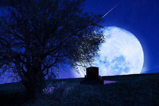 Lonely grave with oak tree under starry and Moonlit night.