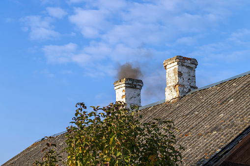 A chimney in a wooden house with black smoke, heating an old wooden house with firewood, the smoke from burning which goes into the chimney
