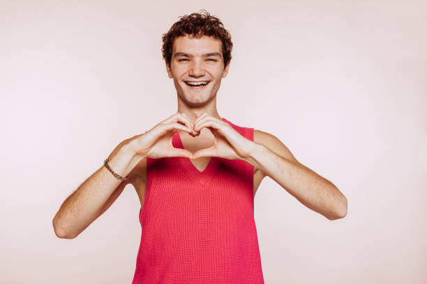 istock Smiling young gay man does heart shape with hands at studio 1449019564