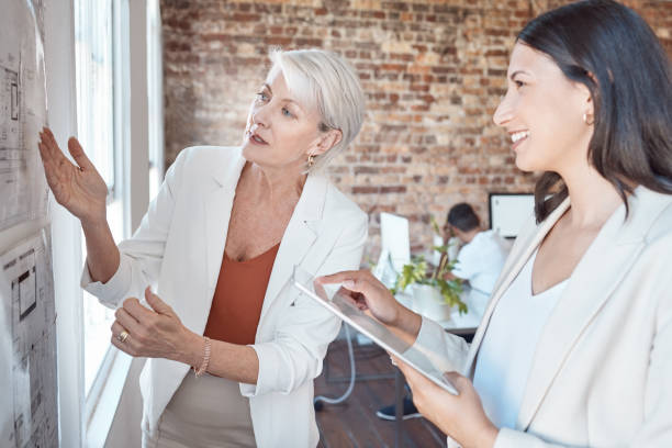 istock Leadership, presentation and coach talking and explaining ideas, vision and strategy plan during a meeting. Senior architect showing blueprint on board during a briefing with employee with a tablet 1449019868