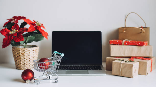 istock Successful Christmas Season in E-Commerce, Christmas online shopping. Open laptop computer Display screen, mini shopping cart, Poinsettias Christmas Flower and gift boxes on white table 1449029977