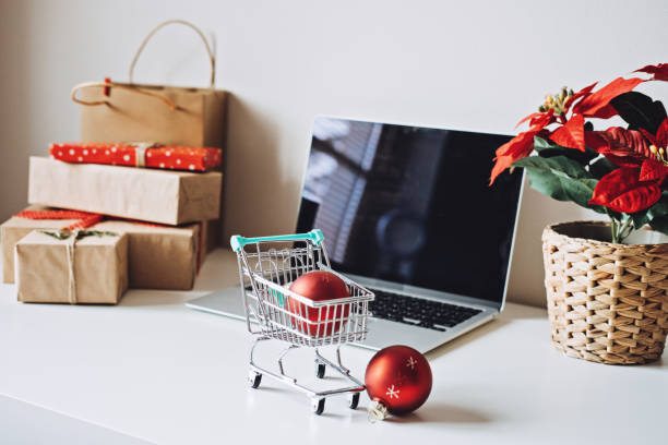 istock Successful Christmas Season in E-Commerce, Christmas online shopping. Open laptop computer Display screen, mini shopping cart, Poinsettias Christmas Flower and gift boxes on white table 1449029982