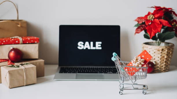 Successful Christmas Season in E-Commerce, Christmas online shopping. Open laptop computer Display screen, mini shopping cart, Poinsettias Christmas Flower and gift boxes on white table