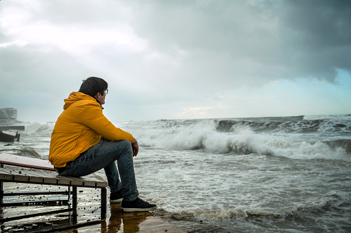Man sitting on a coastline during stormy weather