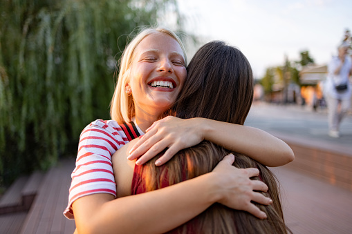 Young happy woman enjoying in a hug with her friend on the street.