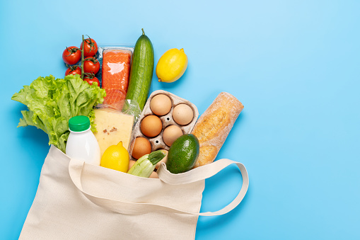 Shopping bag full of healthy food on blue background. Flat lay with copy space