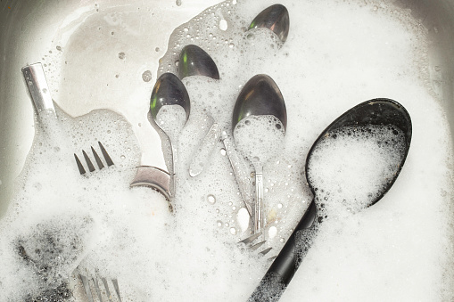 silverware covered in white foam in a steel sink, soft focus close up