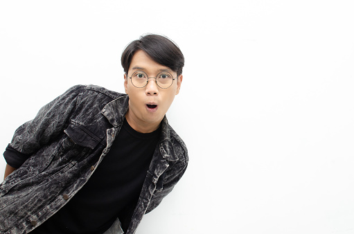 ecstatic attractive young asian man shocked happily opening mouth and lowering glasses. Asian man with glasses expressing shock and surprise with a wow look.
