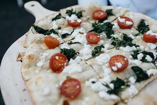 tarte flambée with cherry tomatoes, goat cheese and spinach served on a board