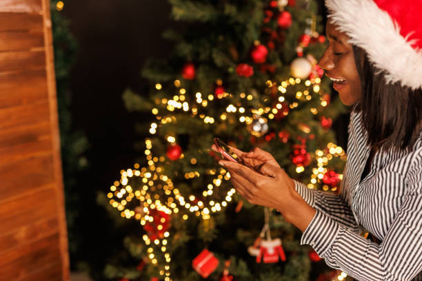 istock Young woman standing by the Christmas tree and using smart phone 1449034968