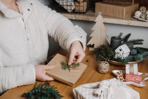 istock Christmas Zero waste eco friendly reuse wrapping gifts process. Woman wrapping Christmas Zero waste reusable craft paper sustainable gifts in craft paper with green leaves on table at home 1449035843