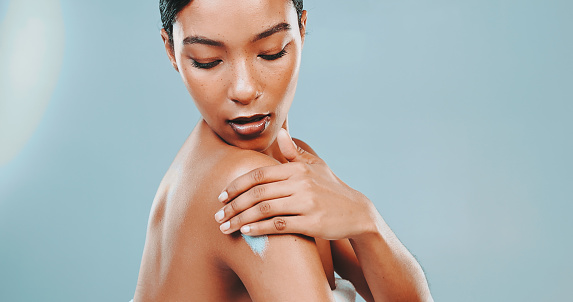 Close-up of attractive young woman applying moisturizer on her arm for soft and glowing skin against blue background