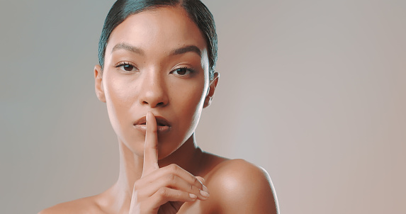 Close-up portrait of beautiful confident African American female model with finger on lips posing against gray background