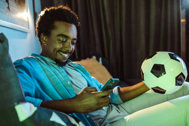 istock Young African American man checking phone while watching sports at home 1449044045