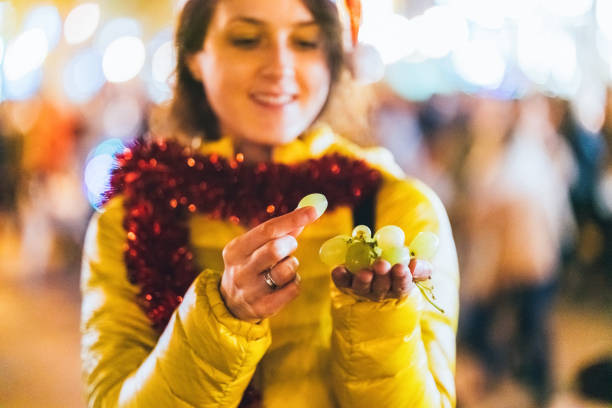 Woman eating grape at New Year's eve in Spain Happy woman celebrating New Year in Valencia and eating grape outside at night new year urban scene horizontal people stock pictures, royalty-free photos & images