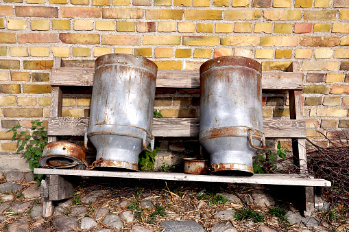 Vintage milk cans up side down om a wooden rack against old brick wall