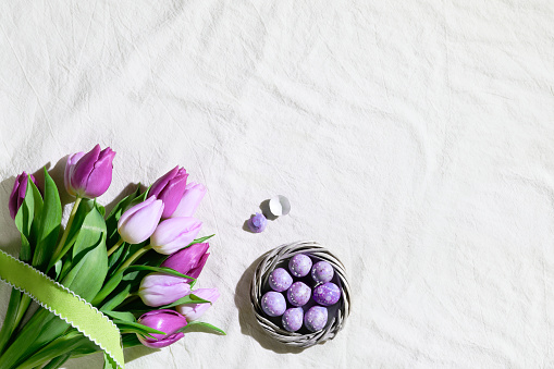 Easter corner composition with bunch of pink magenta tulips and nest, wreath with quail Easter eggs. Flat lay on off white textile tablecloth. Greeting card, webpage design. Copy-space, place for text.