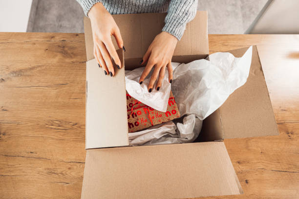 istock Unrecognizable woman, top down view packaging a Christmas present in a larger box, to send with mail 1449063412