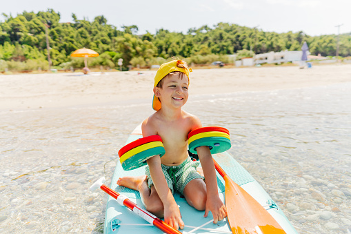 Photo of a smiling boy with water wings sitting on the stand-up paddleboard