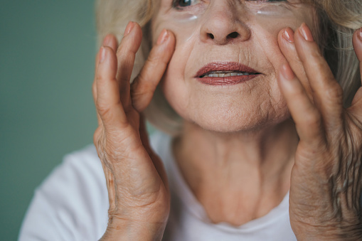 Close-up portrait of retiree woman applying nourishment under eyes patches for looking fresh in morning. Beauty, skin care and old people concept