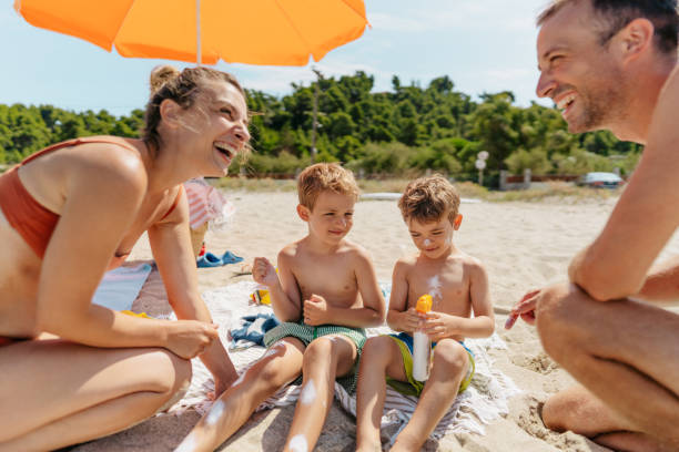 Happy family applying sunscreen while at the beach Photo of a happy family applying sunscreen while at the beach family beach vacations travel stock pictures, royalty-free photos & images