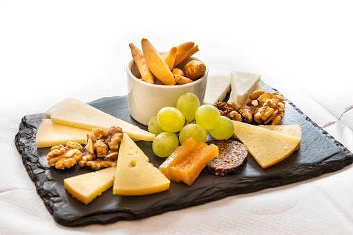 Platter of cheese, cracker, nuts and grapes served on cheeseboard on table with white table cloth