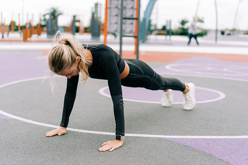 A woman athlete stands in a plank on the sports ground during a workout.