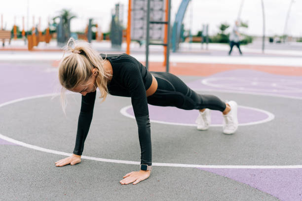 A woman athlete stands in a plank on the sports ground during a workout. A woman athlete stands in a plank on the sports ground during a workout. push ups stock pictures, royalty-free photos & images
