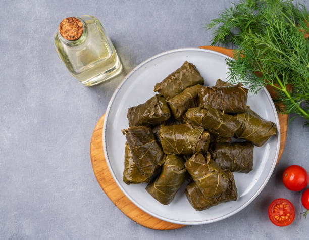 istock Dolma. Stuffed grape leaves (traditional Caucasian, Turkish, Greek cuisine) on a blue plate and cutting board with fresh herbs and tomato on a light background. 1449066547
