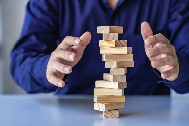 risk management concepts Hands trying to protect the crumbling wooden blocks block tower businessman carefully placed wooden blocks in tall tower Defending the tall wooden tower was also very risky. stock photo