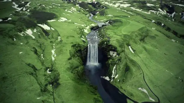 An aerial shot of Skogafoss waterfall surrounded by green highlands in Iceland