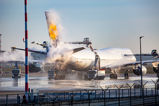 Frankfurt, Germany - December 13, 2022: De-icing of a Boeing 747 of German airline Lufthansa at Frankfurt Airport. In the foreground gantries and trucks of de-icing company NICE. Frankfurt Airport is the largest airport in Germany and serves nearly all international destinations in the world.