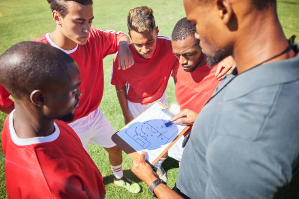 istock Soccer coaching, planning strategy and group sports competition, game and tactical training on outdoor pitch field. Football players manager, teamwork and paper formation, goals and learning sketch 1449076230