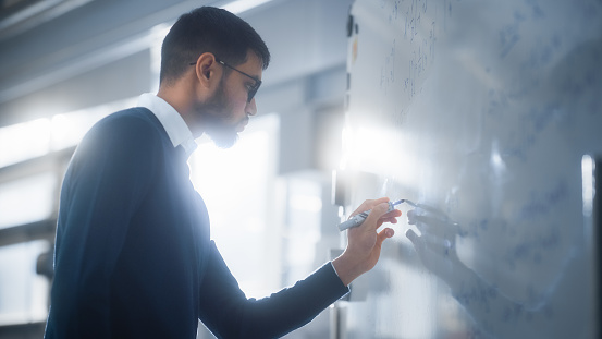 Black Male Scientist Solving Complex Mathematical Problems Standing and Writing Long Formulas on Whiteboard. Higher Education, Science, Technology and Innovation Concept.