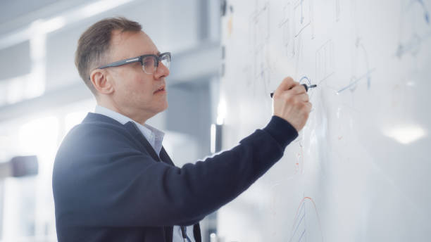 chief engineer drawing graphs on a whiteboard during university lesson in classroom. solving problems and searching new efficient solutions and strategies in engineering concept. - whiteboard education school university imagens e fotografias de stock