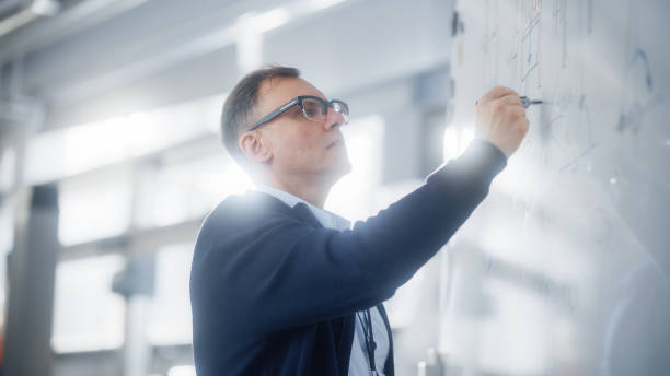 istock Teacher Talks to Students and Use Chalkboard During University Lecture in Classroom. Smart Caucasian Man Draws Formulas and Schemes on Seminar. Genius Solves Problems Concept. 1449083391