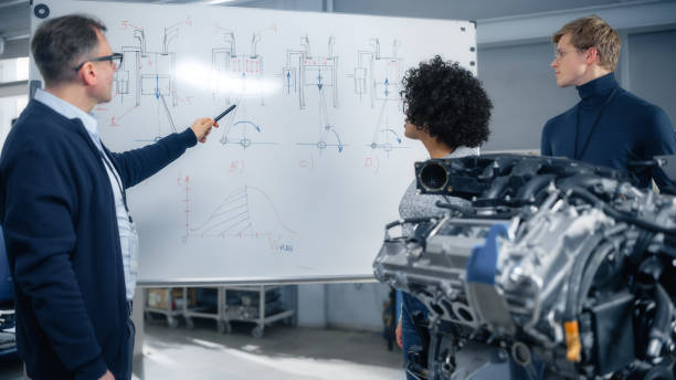 istock Male Teacher Talks About Engineering to Students And Points at Whiteboard. Smart Future Scientists Listen Attentively and Look at Engine. Modern Industry 4 Sustainable Energy Research and Education. 1449083672