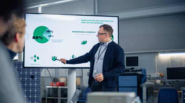 Male Engineer Points at Big Screen With Presentation and Talks About Green Energy and Solar Panels Future Possibilities. Engineering and Sustainable Energy Education Concept.