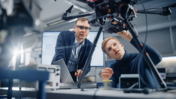 istock Chief Engineer Looks at the Drone Attentively While Discussing Design with Promising Computer Scientist. Manufacturing Facility that Creates Modern Unmanned Aerial Vehicles. 1449083983
