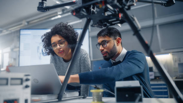 Black Male Engineer Points at Laptop Screen and Talks. Brainstorming New Drone Design With his Female Colleague. Innovative Technologies in Unmanned Aerial Vehicle Design Concept.