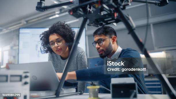 Black Male Engineer Points At Laptop Screen And Talks Brainstorming New Drone Design With His Female Colleague Innovative Technologies In Unmanned Aerial Vehicle Design Concept Stock Photo - Download Image Now