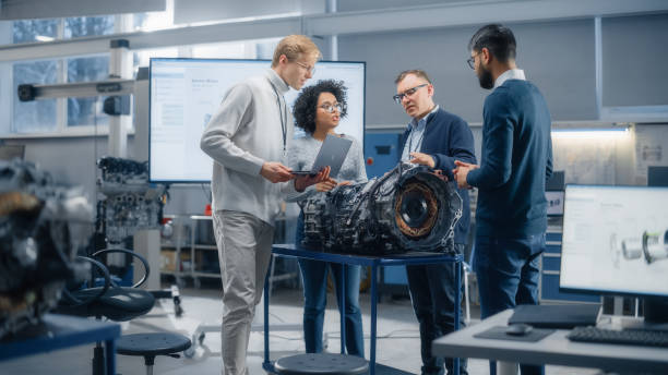 istock Multi Ethnic Group of Young Specialists Talk with Chief Engineer. Professionals Using Laptop and Working on Electric Engine Design. Scientific Startup for Futuristic Sustainable Energy Solutions. 1449084772