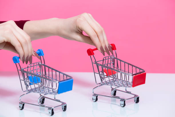 istock Caucasian Female Hand Holding Mockup Small Tiny Shopping Carts Trolley Separately With Both Hands Over Pink Rose Background. 1449085853