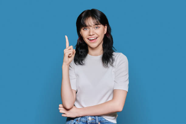 Happy young woman showing index finger up, over blue background stock photo