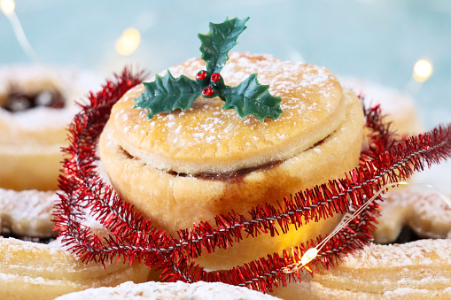 Stock photo showing close-up view of a batch of individual mince pies made with homemade short crust pastry glazed with an egg wash. The pies have been topped with pastry star hole detail lids, hiding the sweet mincemeat (mixture of chopped dried fruit, distilled spirits and spices) filling.