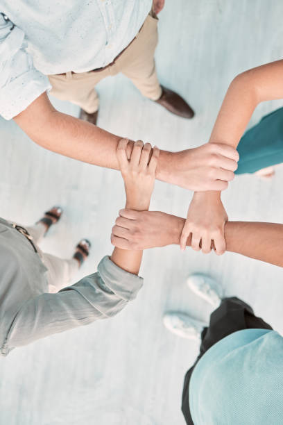istock Hands, collaboration and unity with a business team holding arms in an office together from above. Trust, support and teamwork with a man and woman employee group standing in solidarity or faith 1449087580