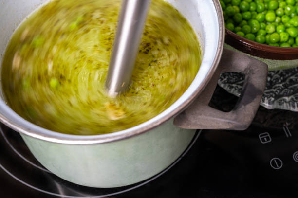 istock Stick blender blends soup in pot on hob, pea. 1449088307