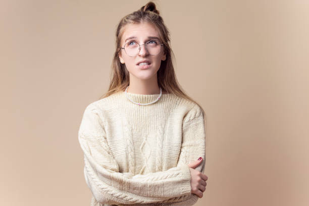 istock Thinking Caucasian Blond Female Wearing Knitted Warm Sweater And Glasses while Curiosly Looking Straight with Lifted Finger And Smile Over Beige. 1449088947