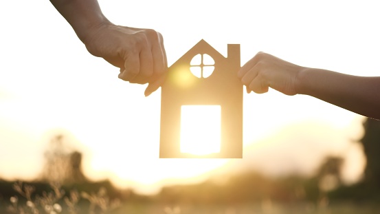 mother and daughter hands holding paper house, home together against sunset with soft focus. Concept of Happy Family, Buy House, Home, life, insurance, care, saving, mortgage, estate