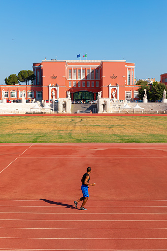 Runner athlete on running track in the “stadio dei marmi” (Stadium of the Marbles) in front of CONI palace (Comitato Olimpico Nazionale Italiano)